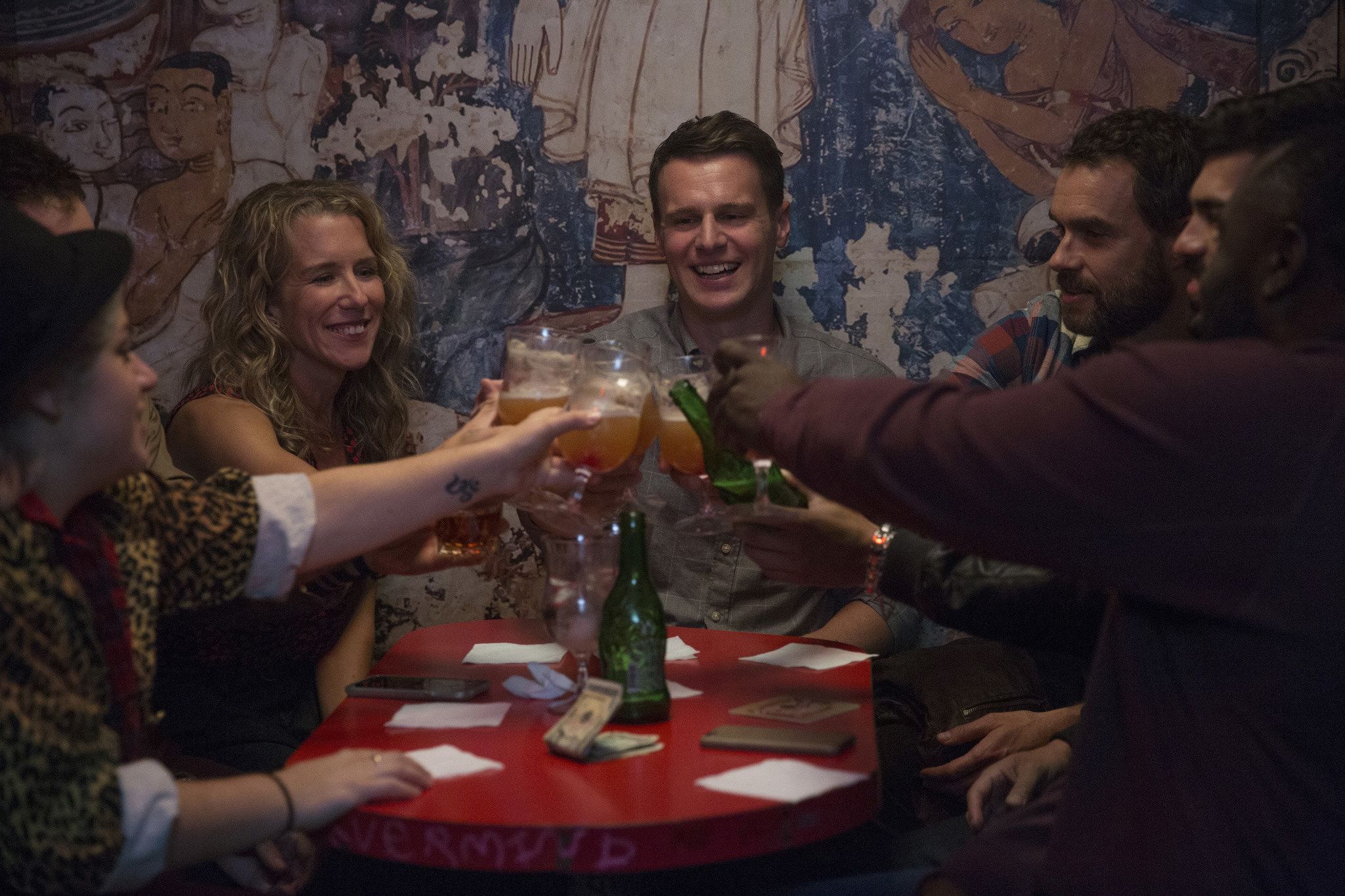 The cast of Looking : The Movie sitting at a table and clinking their glasses while smiling