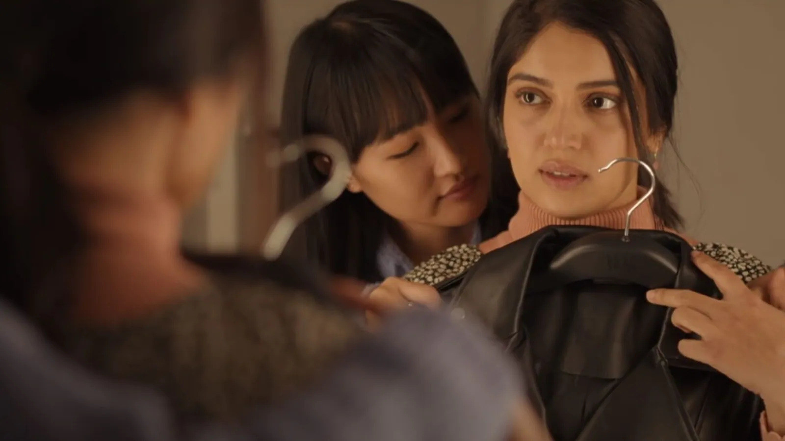 Sumi (Bhumi Pednekar) holding a leather jacket and looking in the mirror with Rimjhim (Chum Darang) behind her