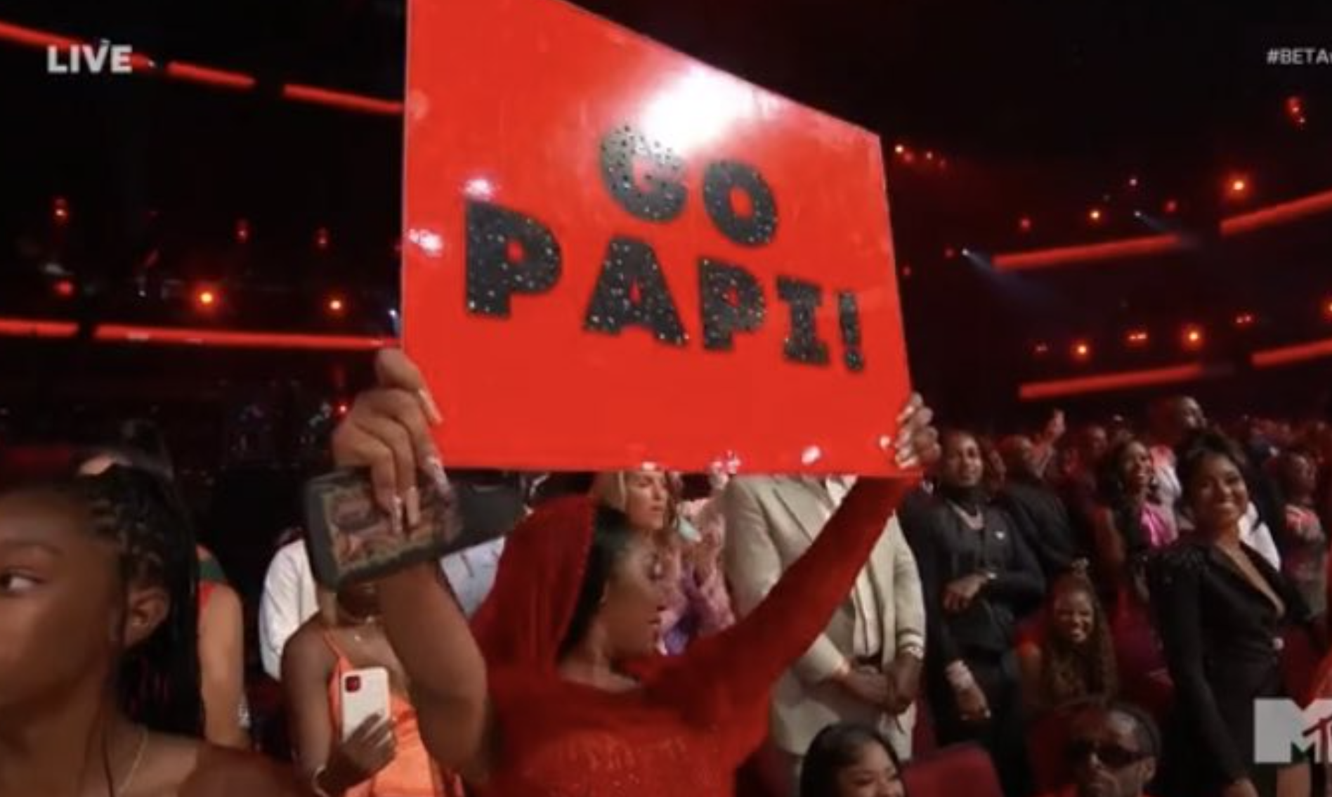 Yung Miami holds a sign that says Go Papi on it