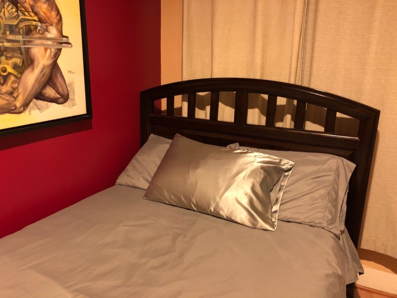 Reviewer&#x27;s photo of the grey satin pillowcase on pillow resting on bed