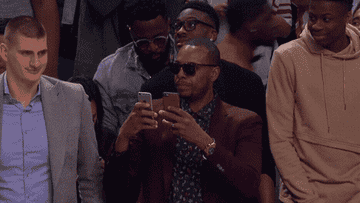 Someone on the sidelines of an NBA game scrolling through two phones at once
