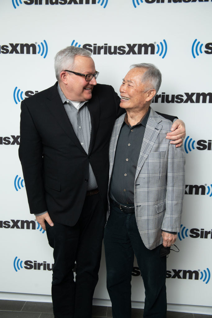 Brad and George Takei smiling and looking at each other