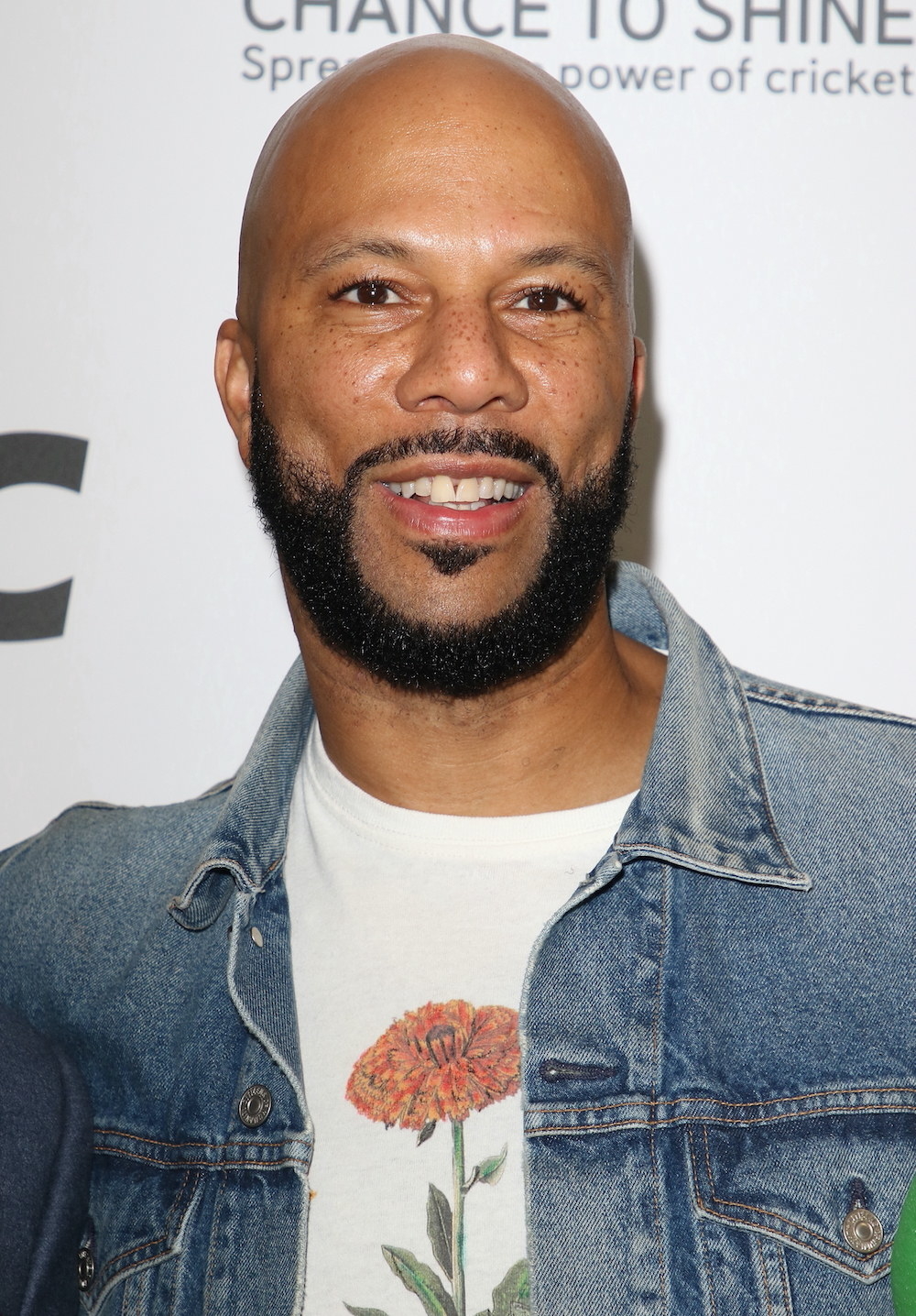 Smiling Common in a beard and mustache and wearing a denim jacket
