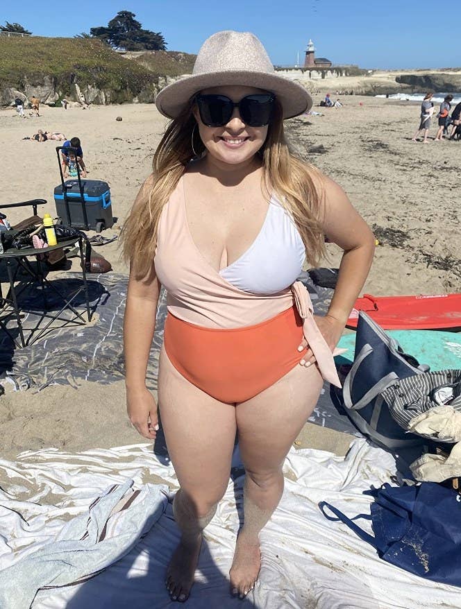 A reviewer wearing an orange/white color block tie one piece swimsuit
