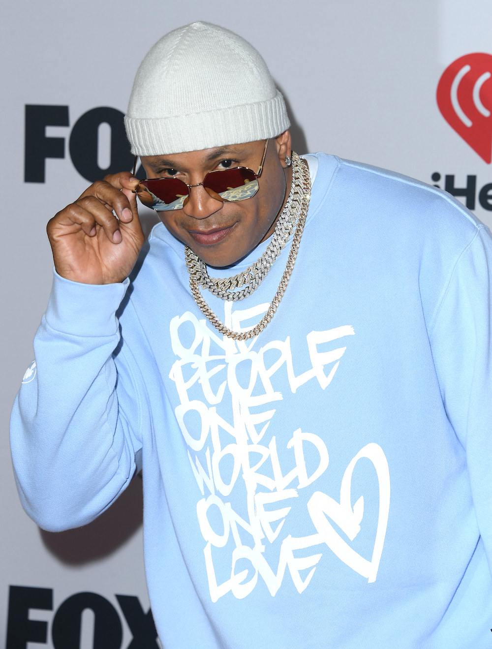 LL in a cap, glasses, thick chain necklaces, and sweatshirt that says &quot;One people one world one love&quot;