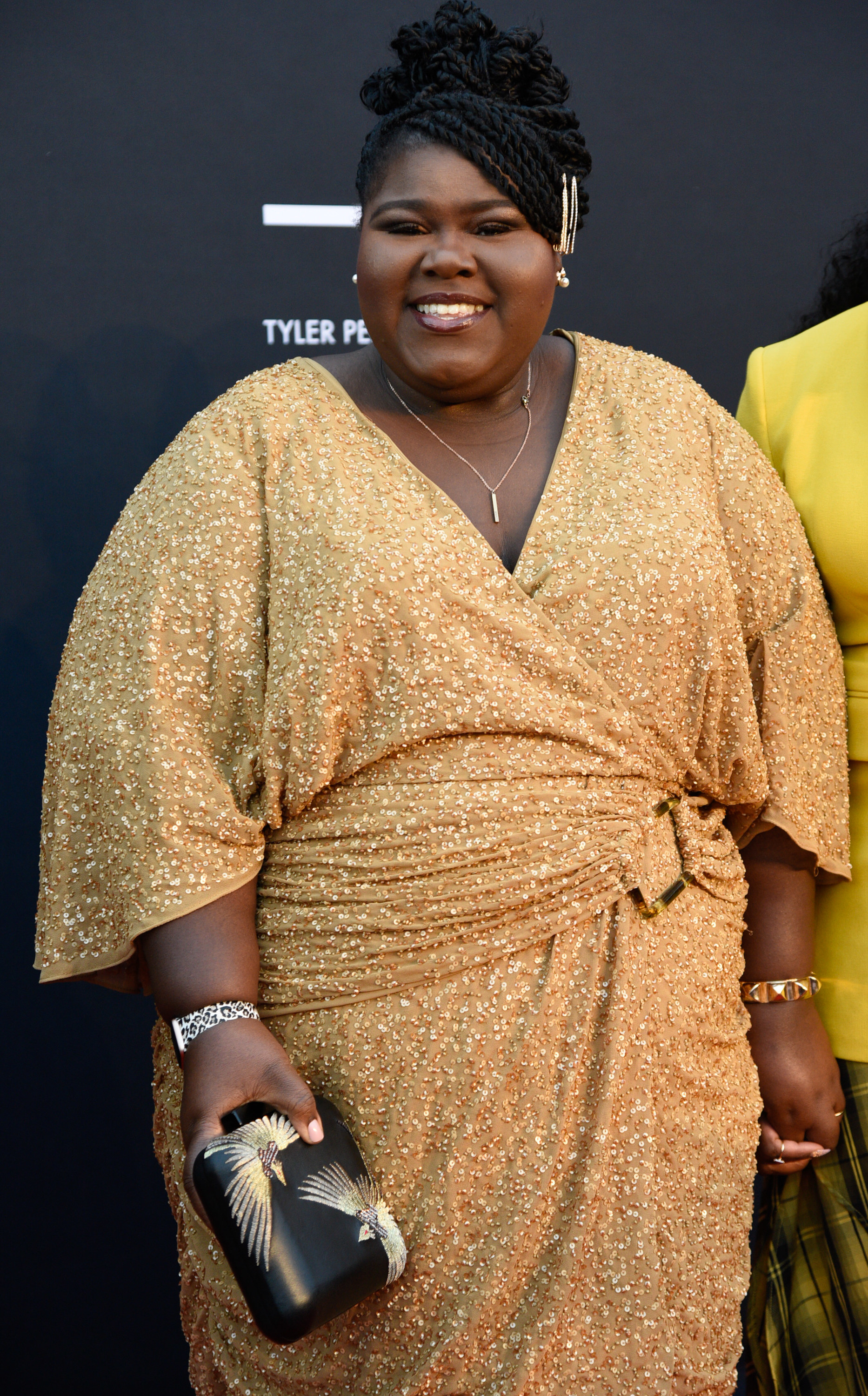 Gabourey smiling in a beaded wrap V-neck dress and a braided updo
