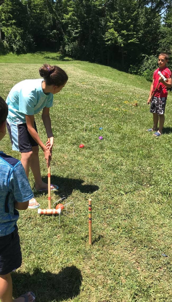 Two children play croquet outside, one about to strike the ball
