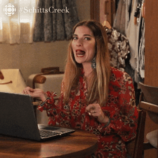 alexis from Schitt&#x27;s Creek in front of a computer happily flipping her hair