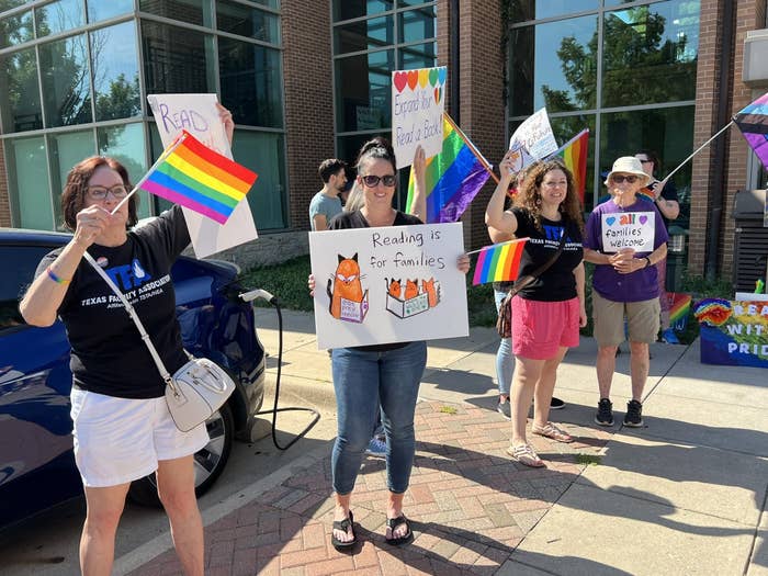 People hold rainbow flags and signs that say "reading is for families" and "all families welcome"