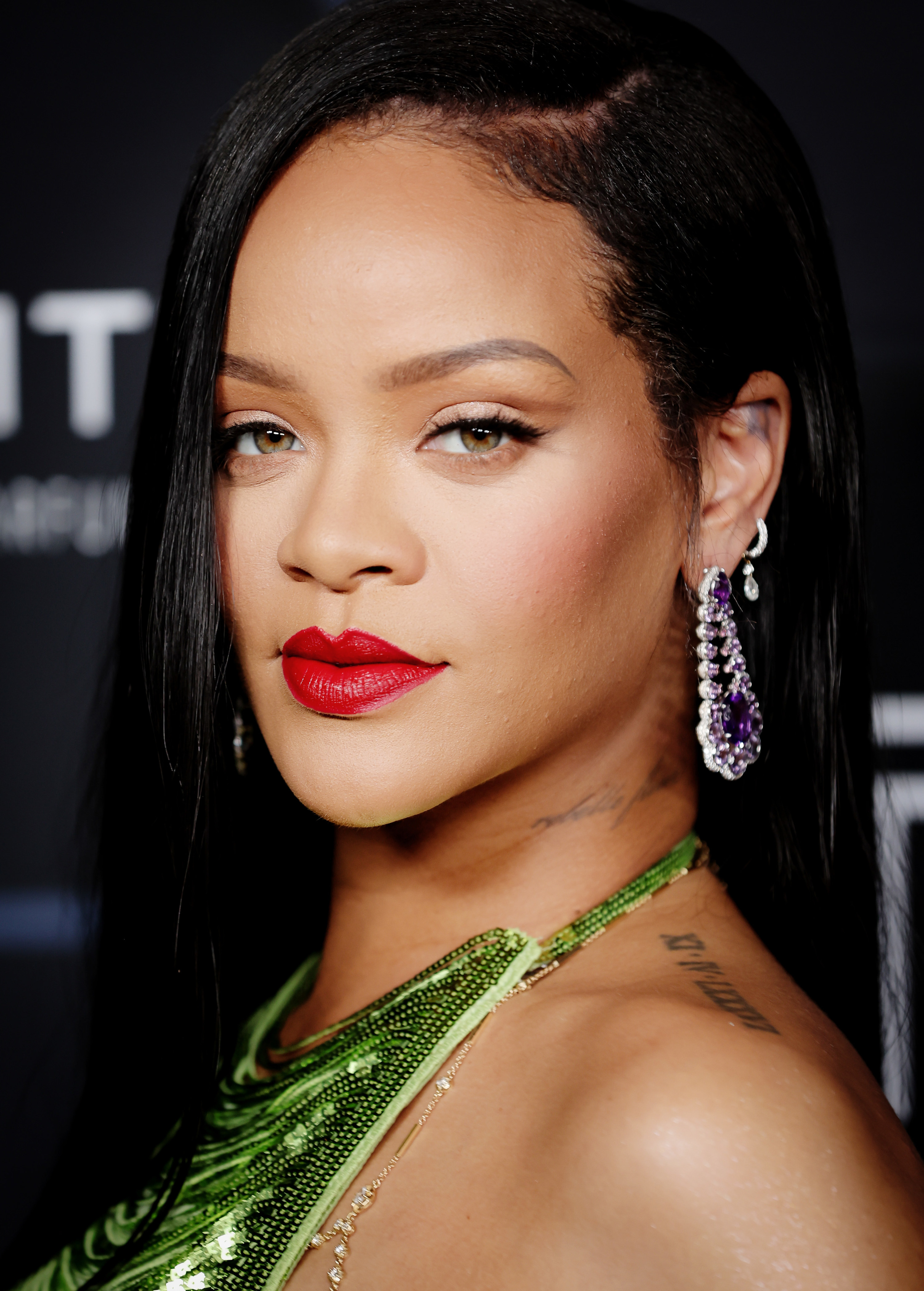 Rihanna smirking at the camera wearing bright red lipstick and a green dress