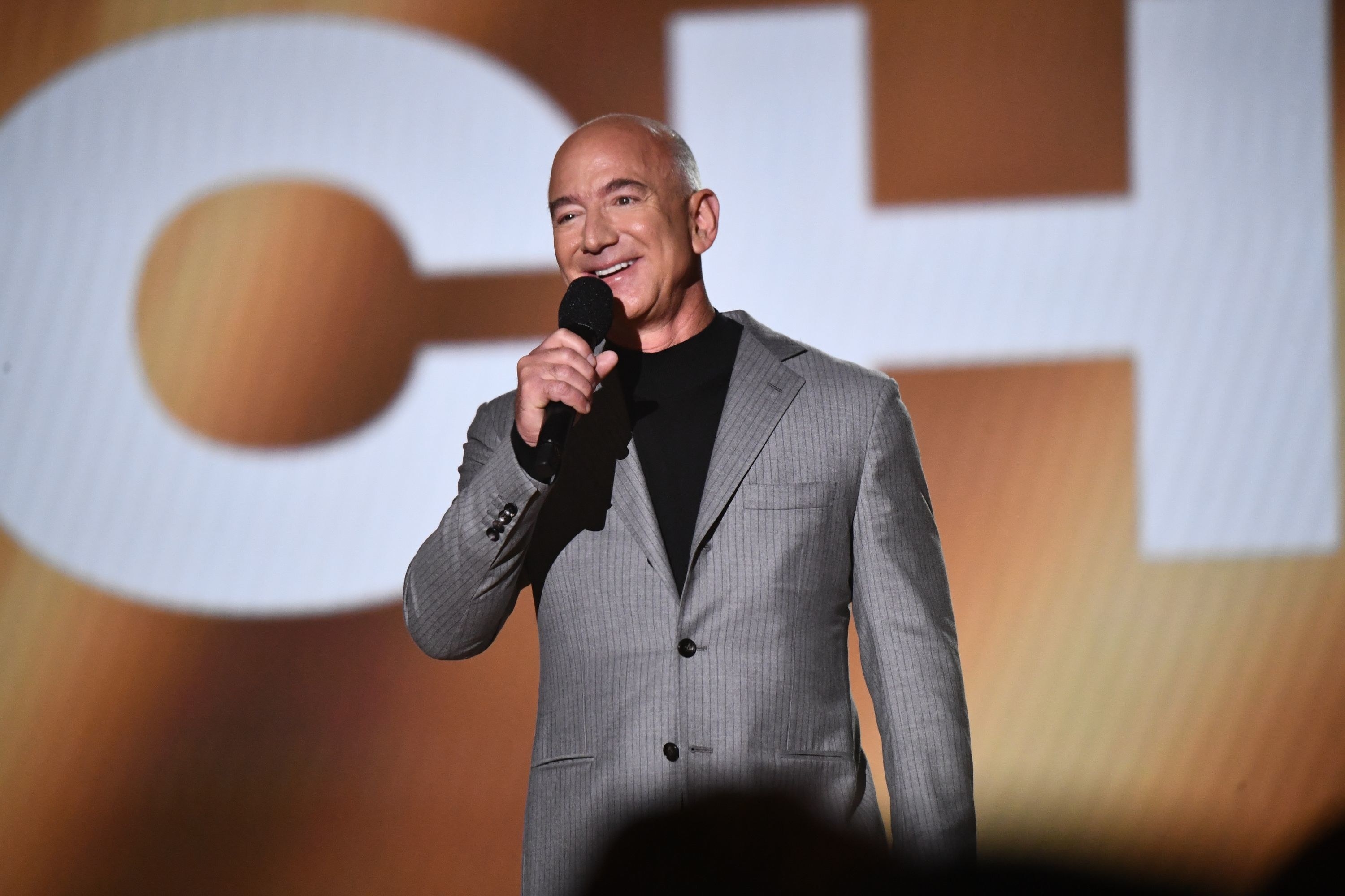 Jeff Bezos giving a speech on stage holding a microphone