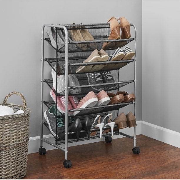 The shoe rack filled with different types of shoes, set on castor wheels in the corner of the room