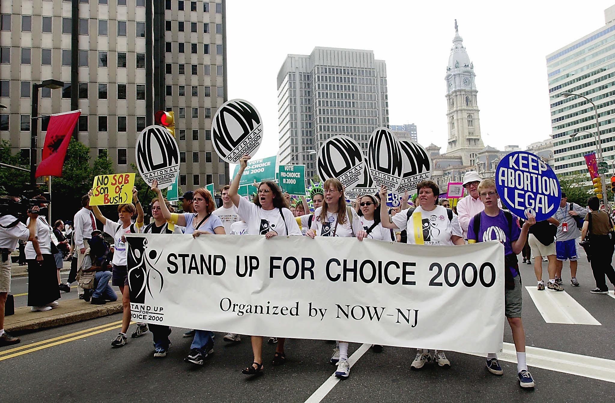 People march in the street holding a banner &quot;stand up for choice 2000&quot;