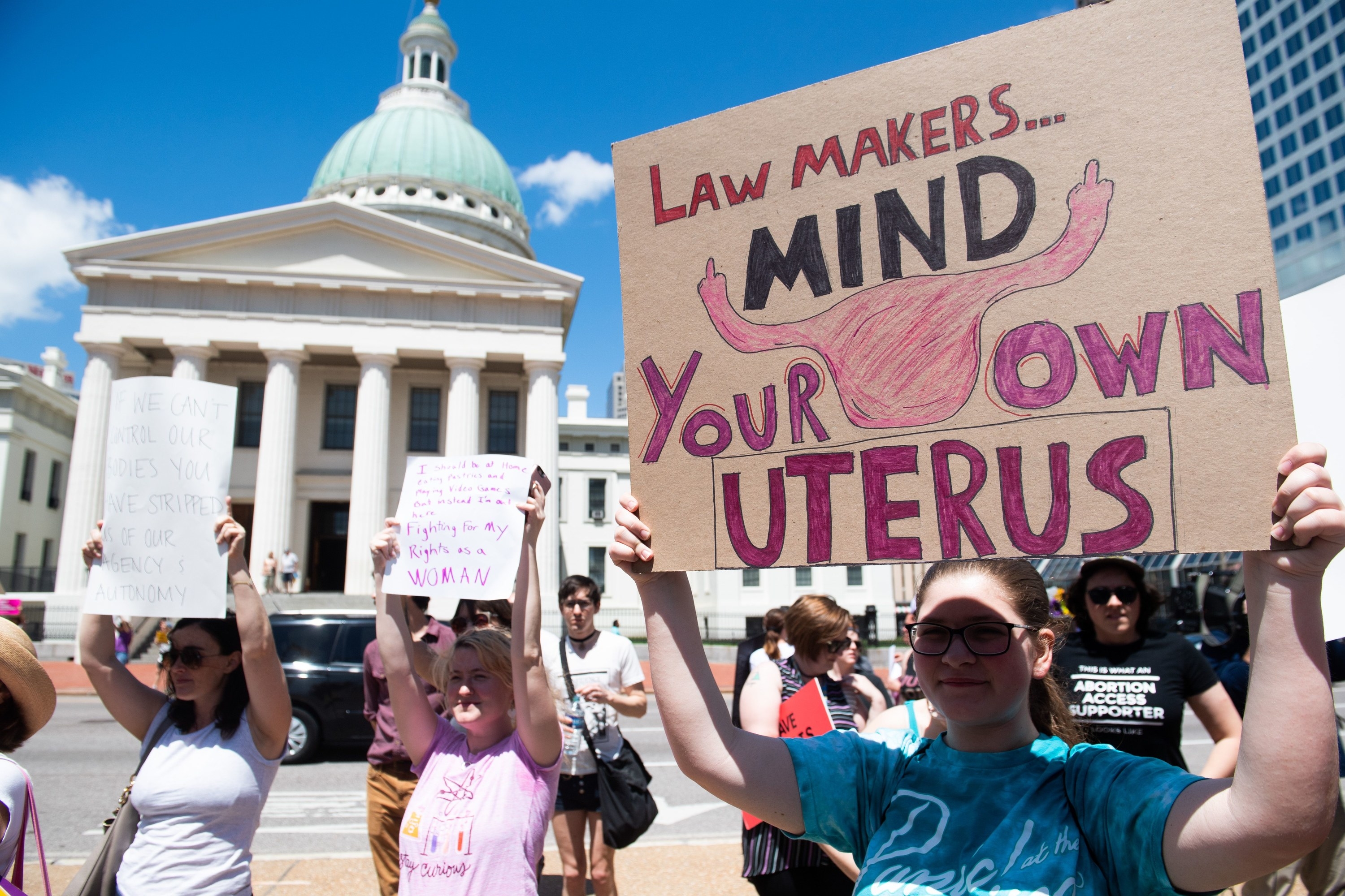 Demonstrators standing in front of a government building hold signs that read &quot;lawmakers, mind your own uterus&quot;