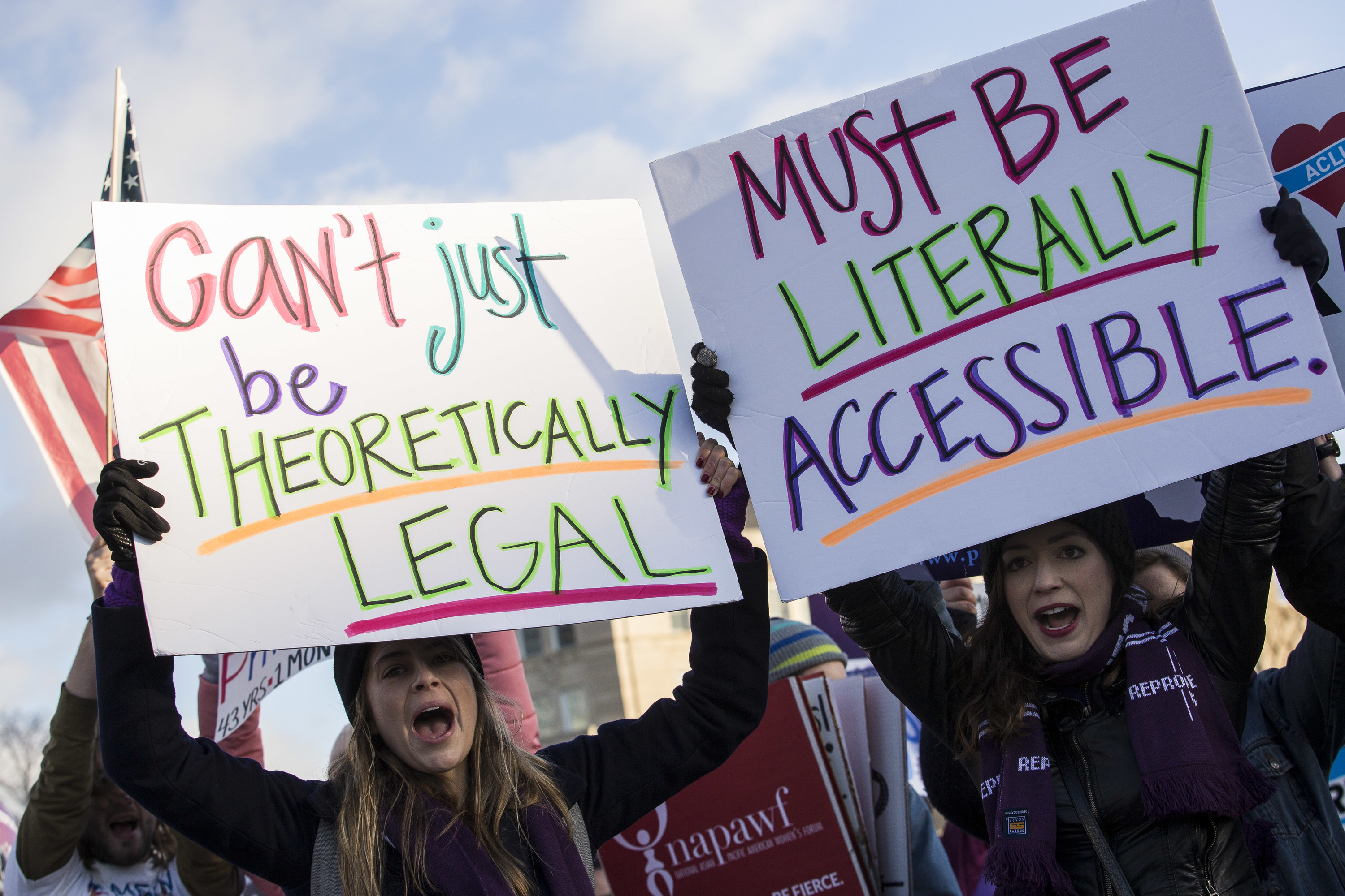 Demonstrators hold signs reading &quot;can&#x27;t just be theoretically legal&quot; and &quot;must be literally accessible&quot;