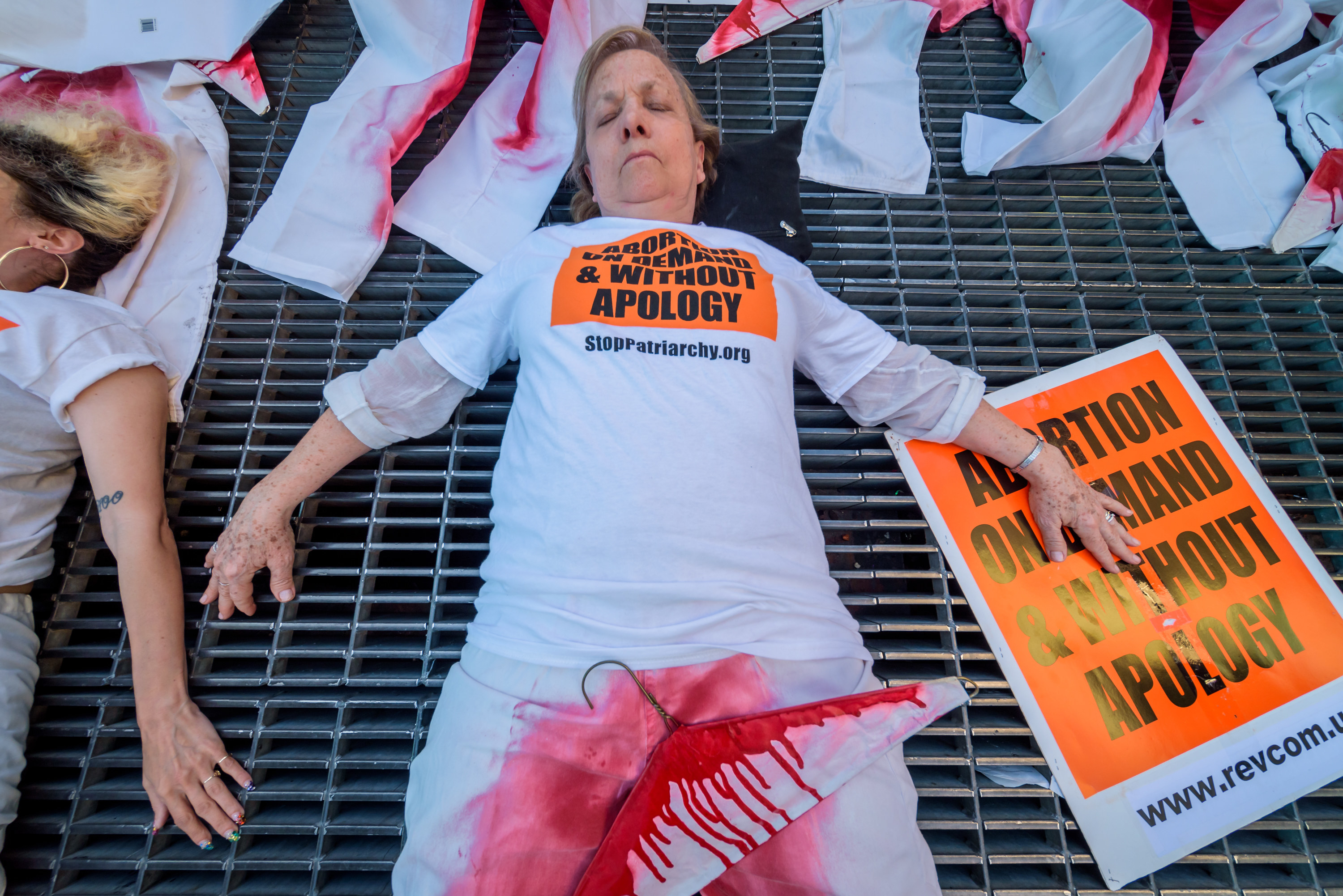 People lie on the ground with red-stained jeans and bloody coat hangers near signs reading &quot;abortion on demand and without apology&quot;