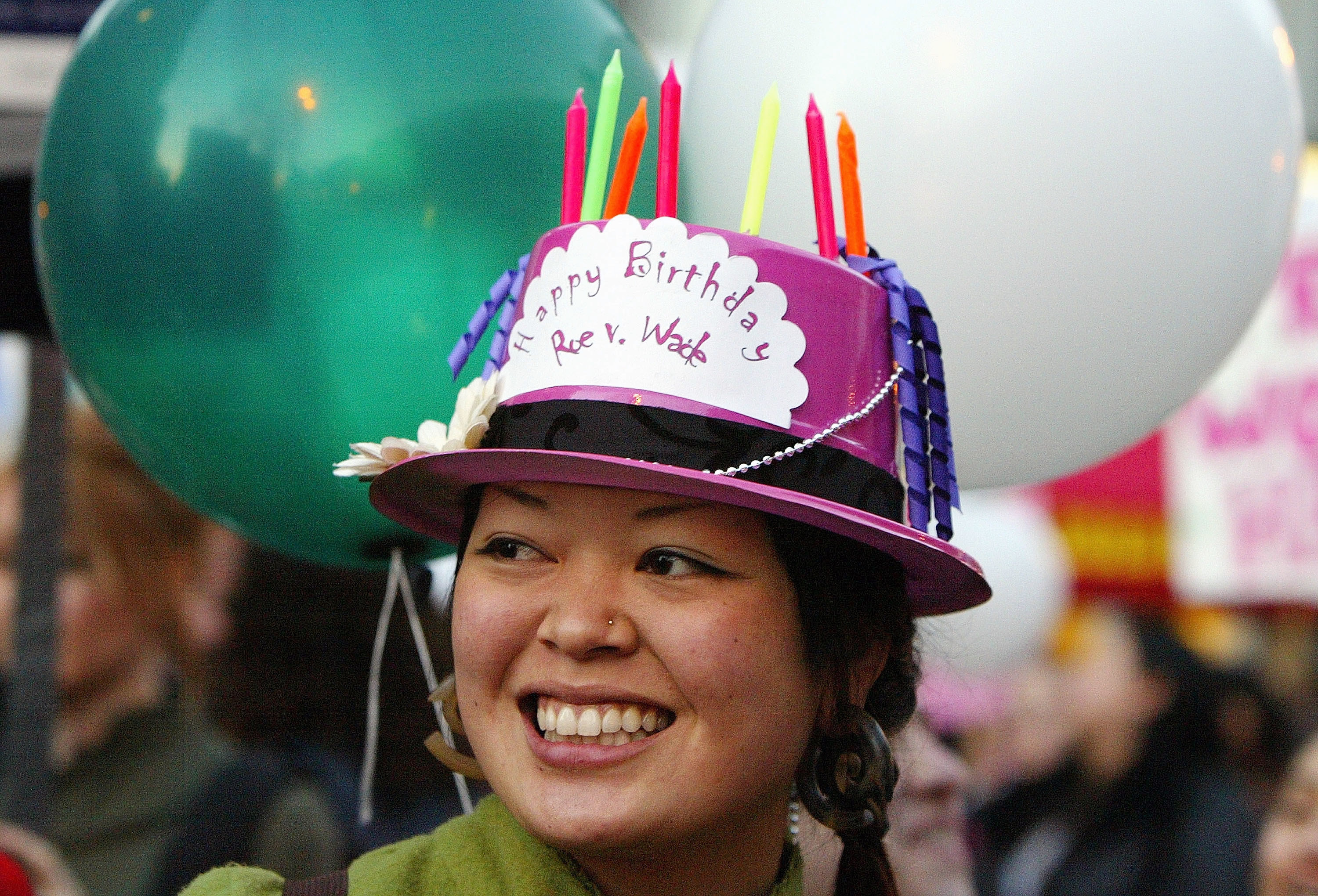 A person wears a hat with birthday candles and a small paper decoration reading &quot;happy birthday roe v wade&quot;