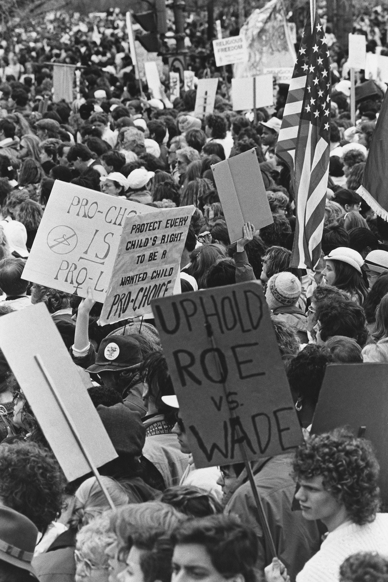 Demonstrators in a large crowd hold signs reading &quot;uphold Roe v Wade&quot; and &quot;protect every child&#x27;s right to be a wanted child&quot; and &quot;pro-choice is pro-life&quot;