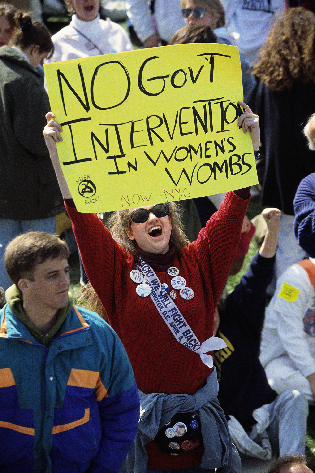 A woman with a wide mouth holds up a bright yellow sign reading &quot;no government intervention in women&#x27;s wombs&quot;
