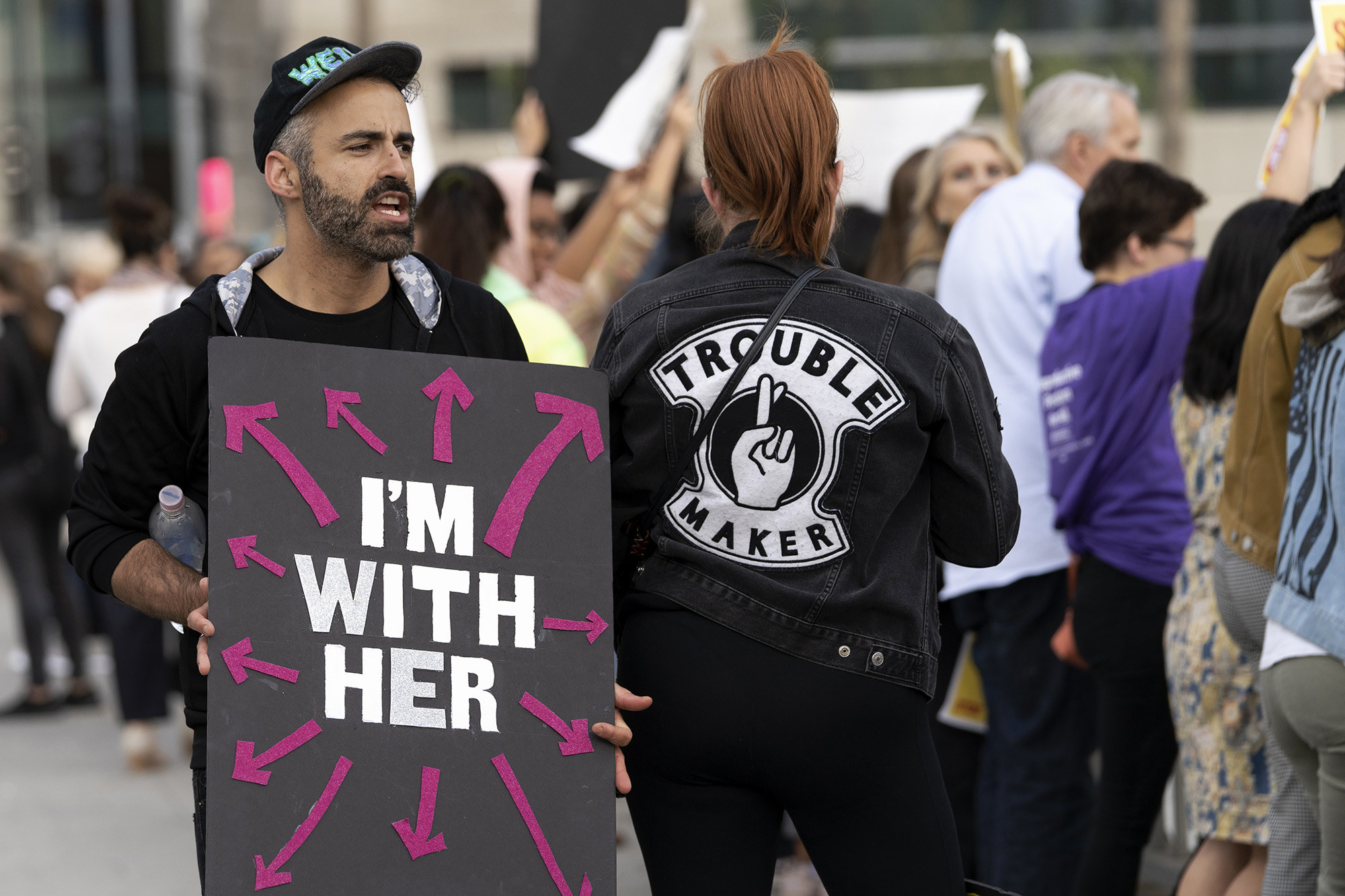 A demonstrator holds a sign reading &quot;I&#x27;m with her&quot; with arrows pointing in all directions