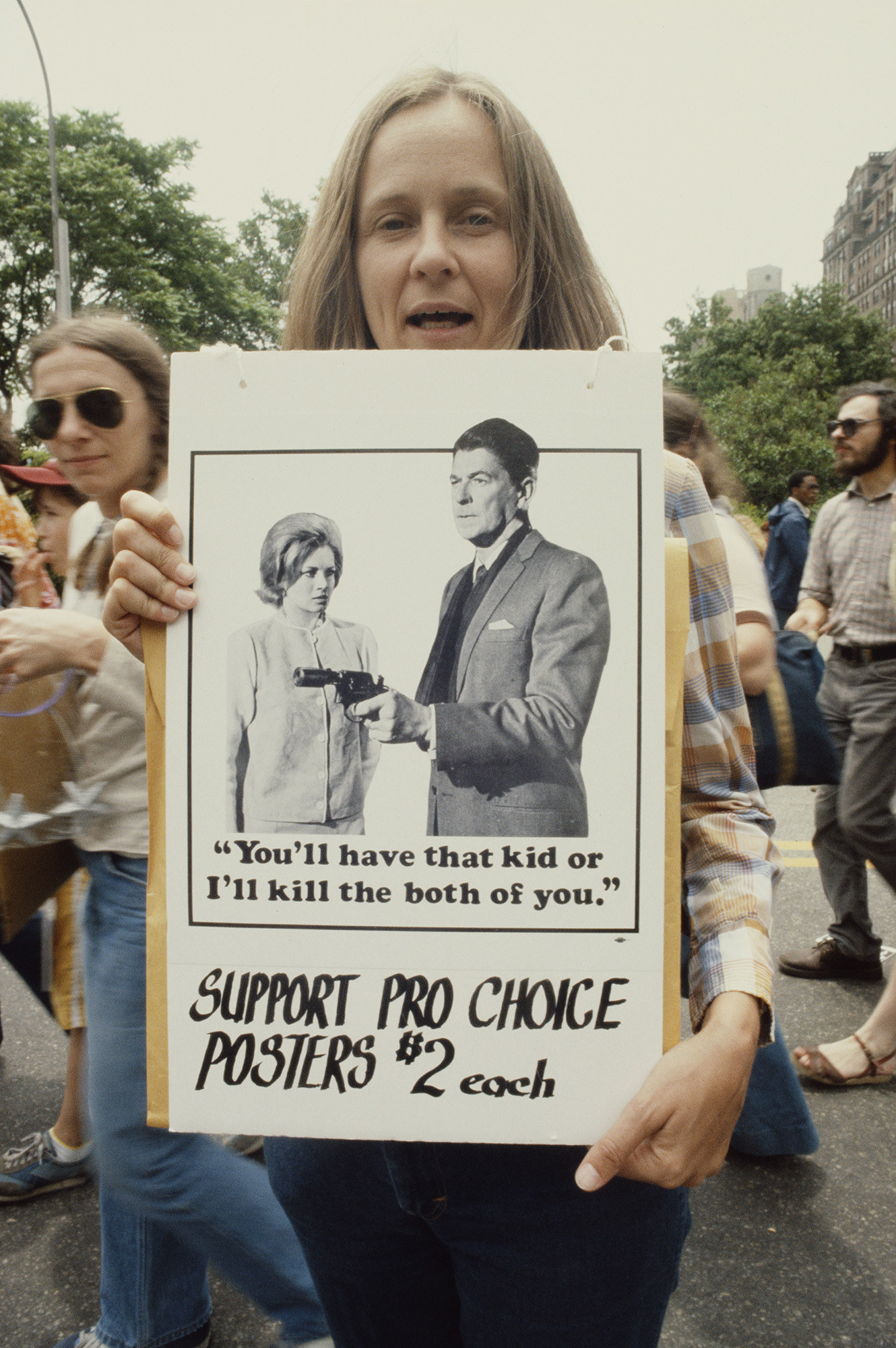 A demonstrator&#x27;s sign shows Ronald Reagan holding up a gun with the text &quot;You&#x27;ll have that kid or I&#x27;ll kill the both of you&quot;