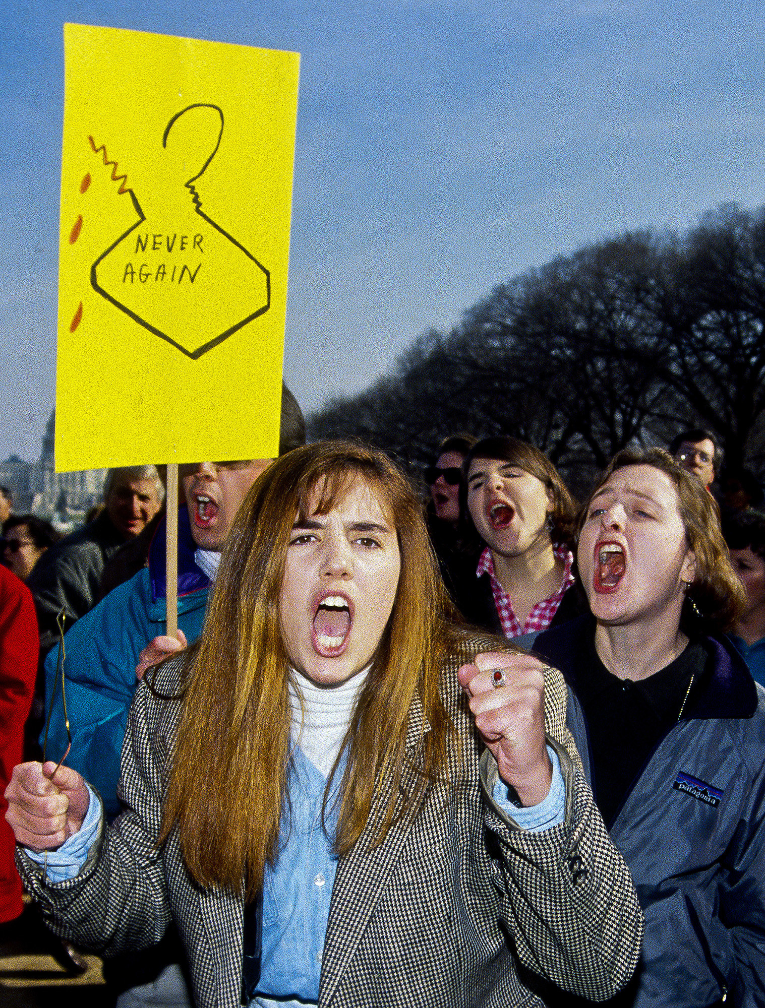 Protesters hold a sign with a broken wire coat hanger reading &quot;never again&quot;