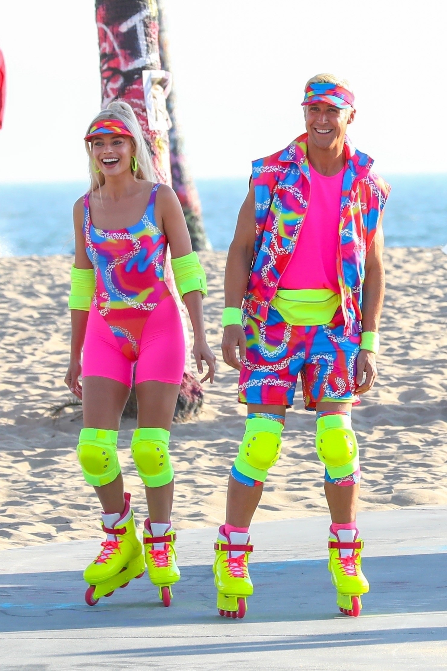 Ryan and Margot wearing matching outfits with bright colors that look like they&#x27;re from the &#x27;80s, as well as matching knee pads and rollerblades