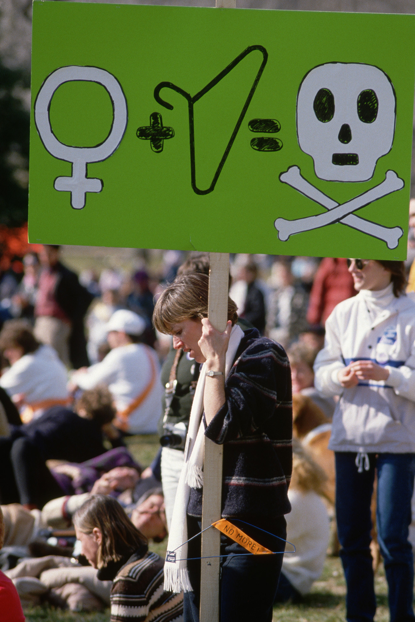 A protest sign shows an equation of a gender glyph denoting women plus a coat hanger equals death, represented by a skull and crossbones