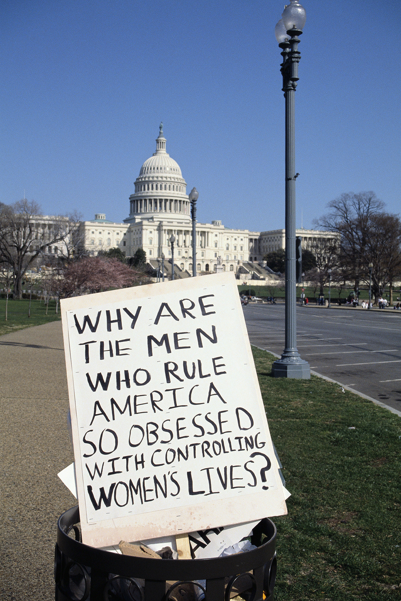A sign in a garbage can reads, &quot;Why are the men who rule America so obsessed with controlling women&#x27;s lives?&quot;