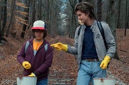 Dustin and Steve from Stranger Things talking as they walk on some railroad tracks in the woods