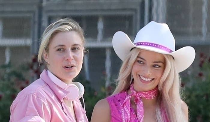 Greta Gerwig standing next to Margot Robbie, who is dressed like Barbie and wearing a cowboy hat