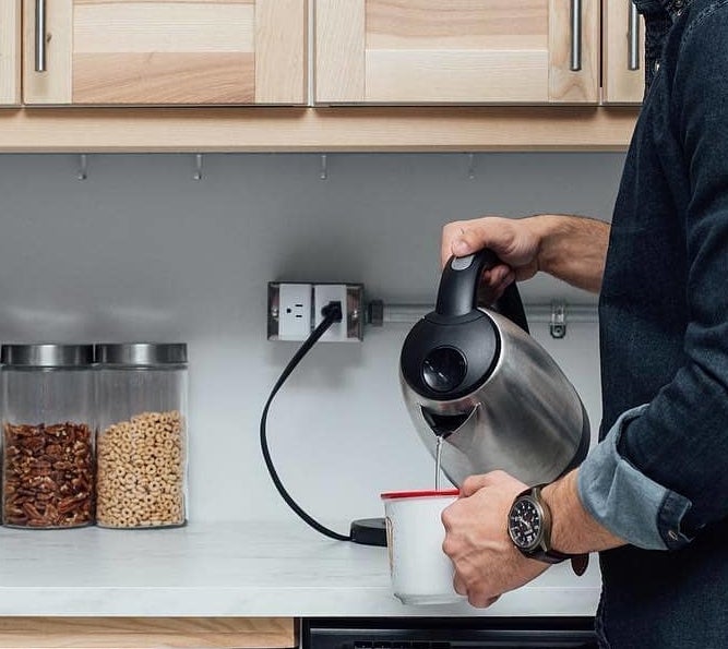 a person pouring water from a kettle that&#x27;s plugged into the smart plug