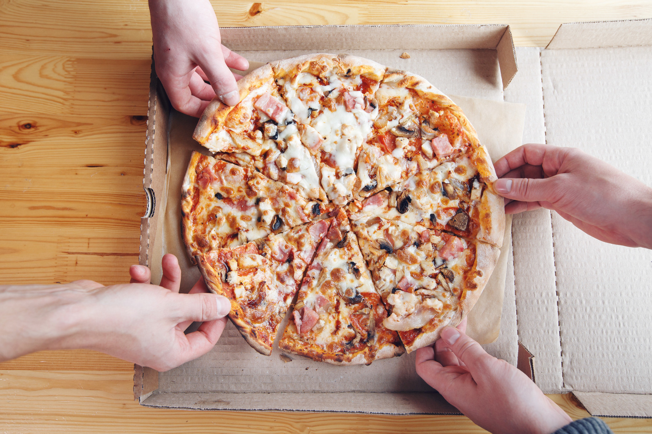 Hands grab slices of delivery pizza