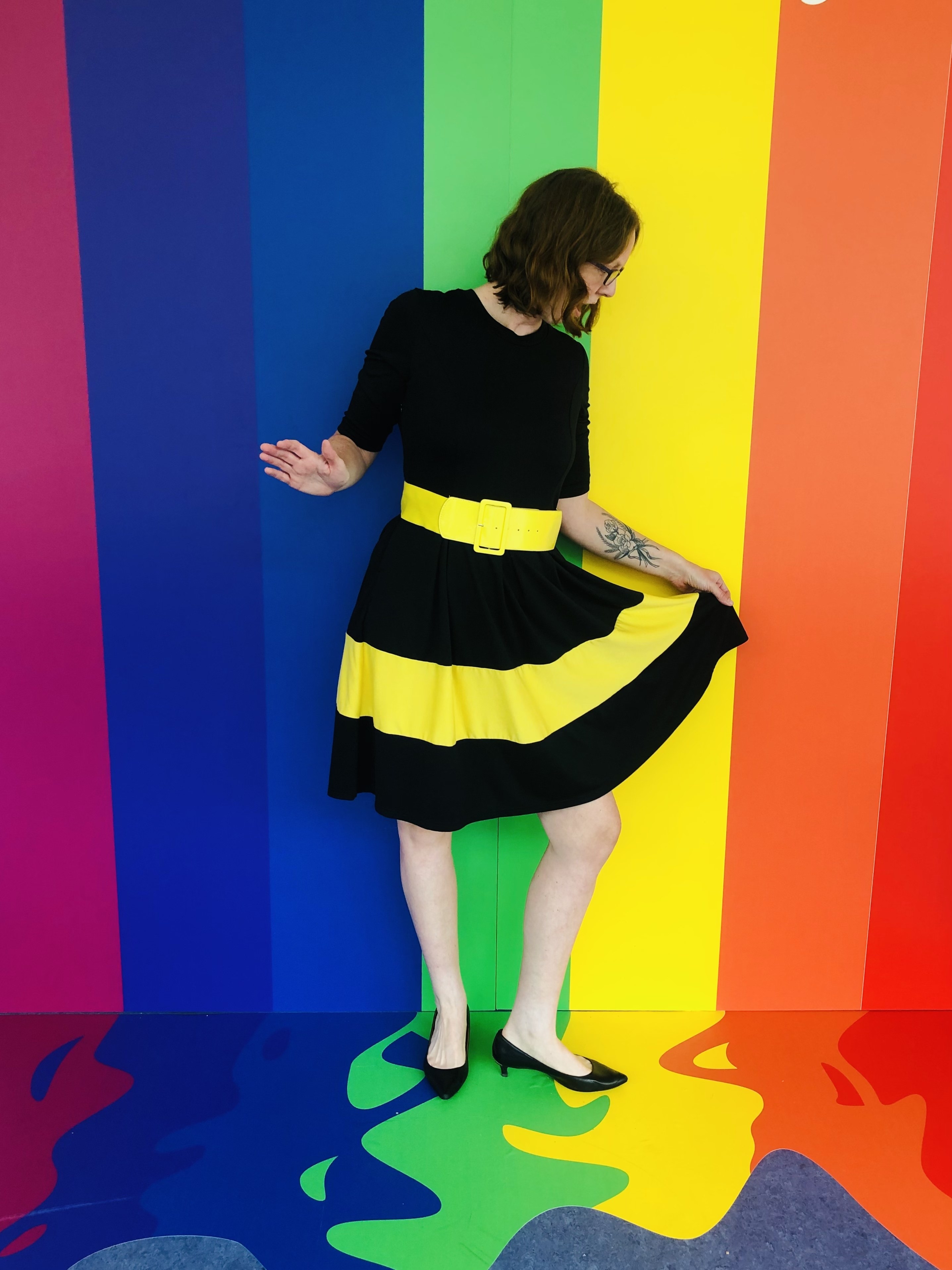 a reviewer wearing the black dress with a yellow stripe in front of a rainbow wall