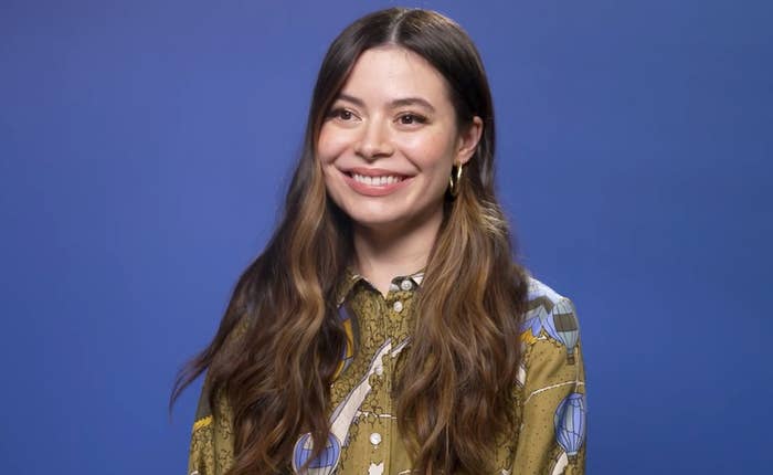 Miranda Cosgrove sitting in front of a blue backdrop looking stunning
