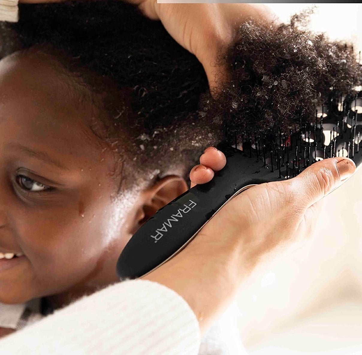 A person combing through a child&#x27;s curly hair with the brush