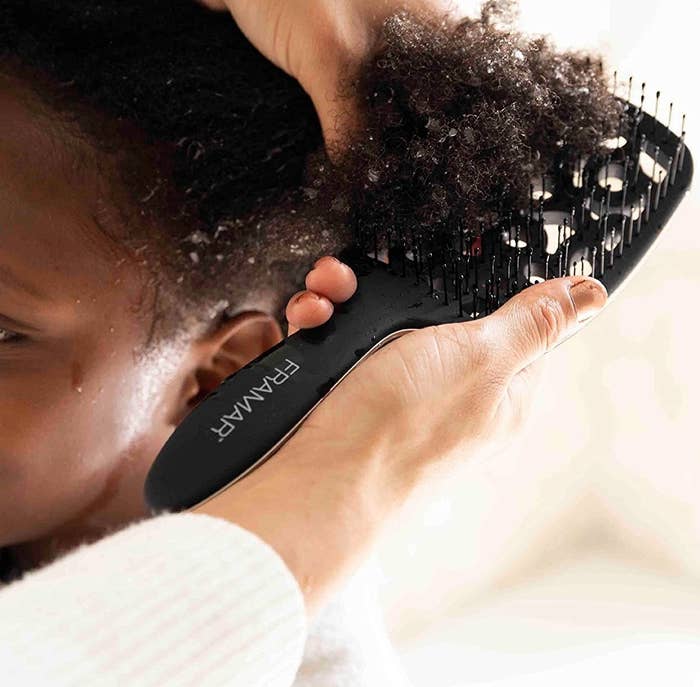 A person combing through a child&#x27;s curly hair with the brush