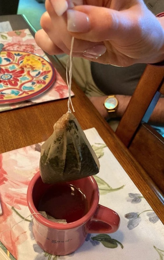 A reviewer showing a full tea bag above a red mug