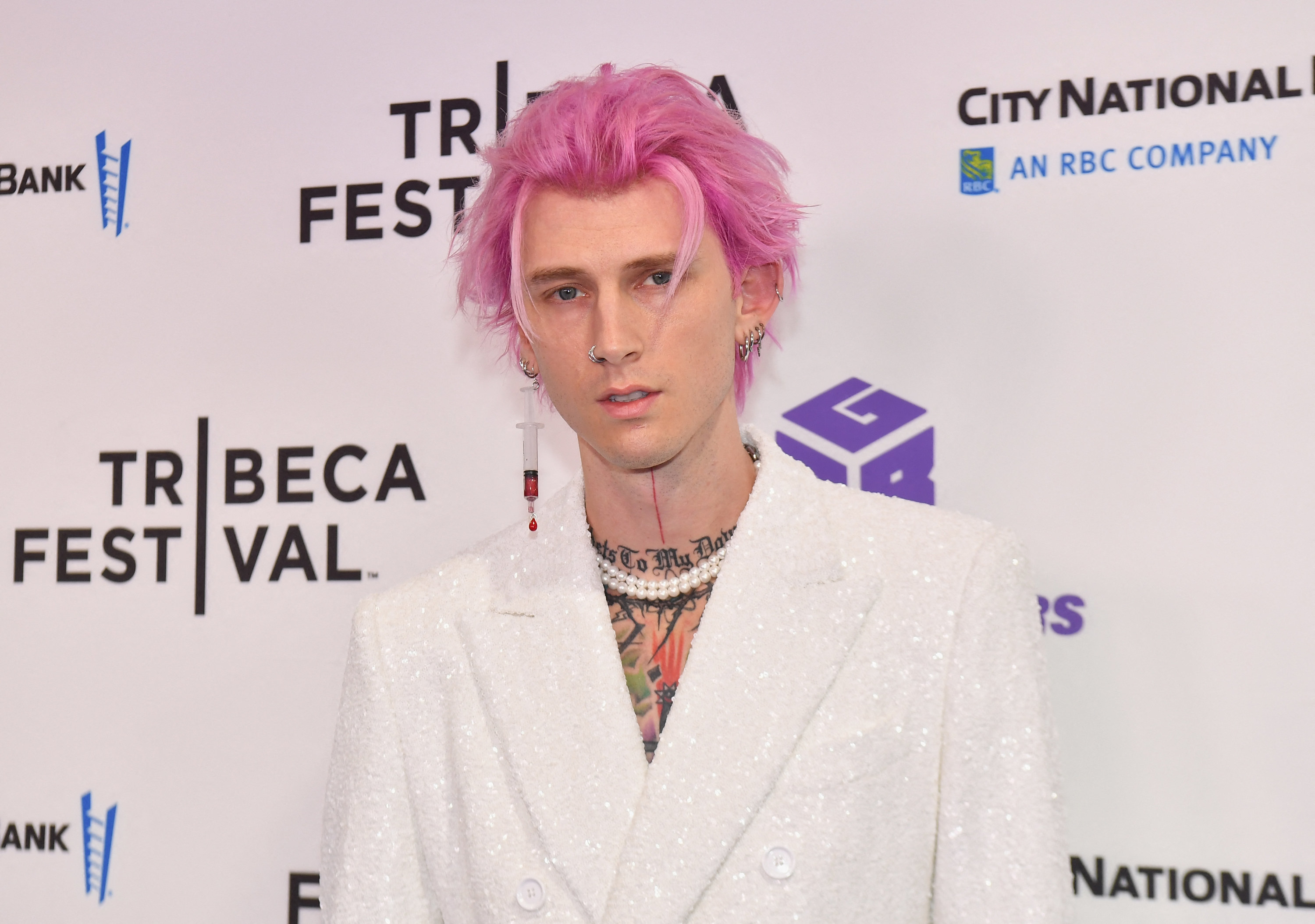 MGK posing on the red carpet, his hair long and his suit beaded
