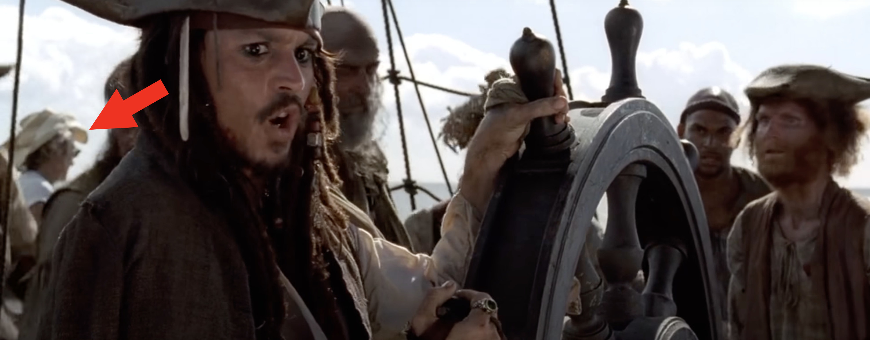 A man with a straw hat stands on deck with Jack Sparrow and his crew