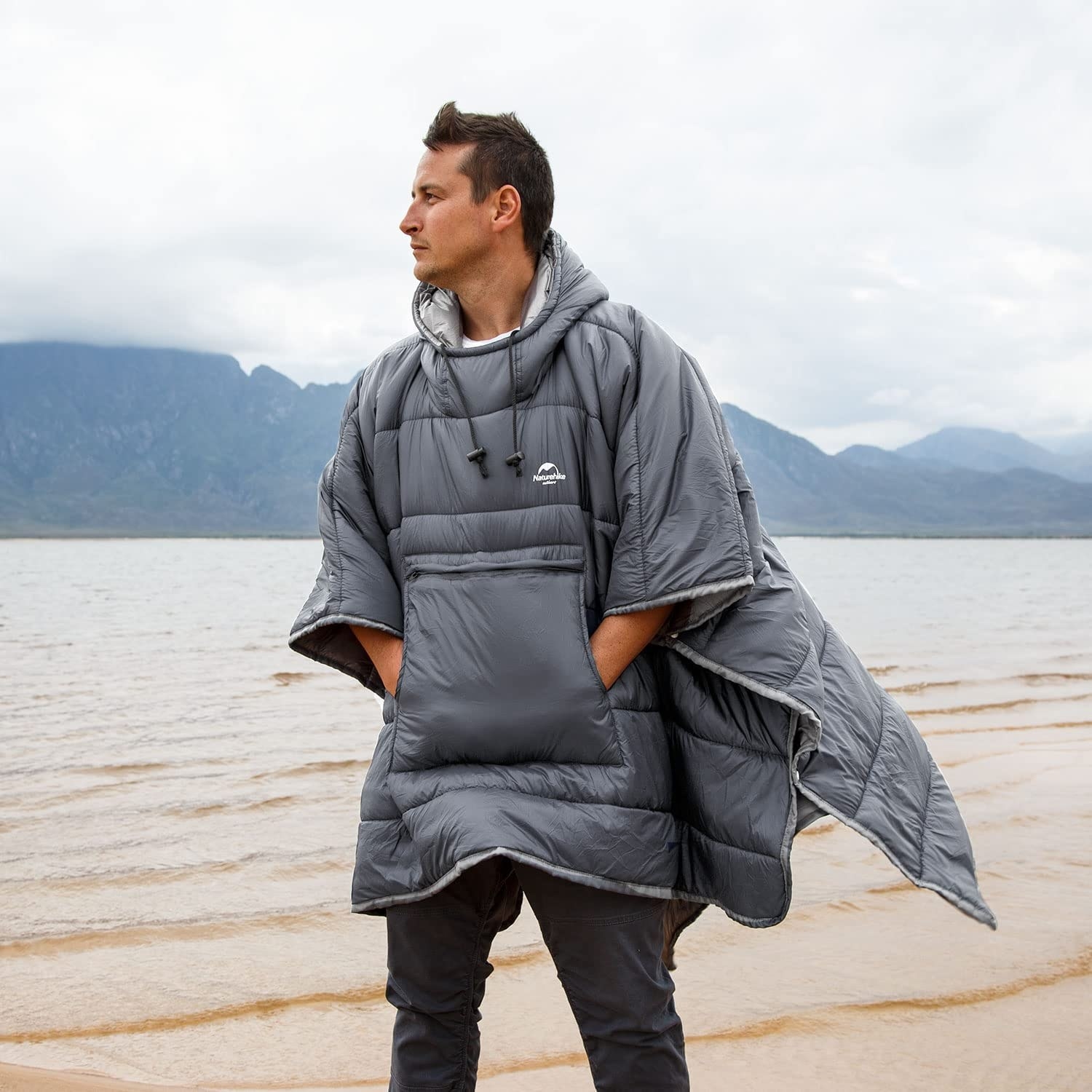a person wearing the sleeping bag poncho while standing lakeside