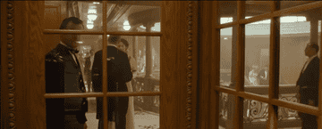 A man opens a glass door and the camera is in the reflection