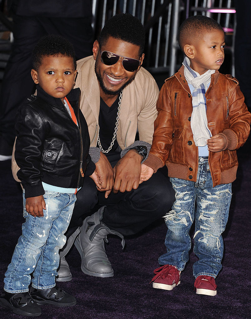 Usher bending down to take a photo with his two toddler sons
