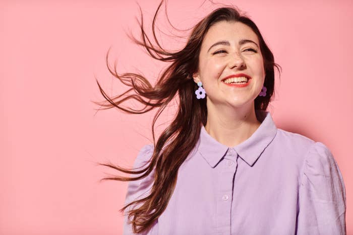 Close up of happy young woman with profound deafness in lilac shirt standing against pink background laughing