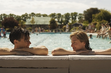 emma corrin and harry styles looking at each other from the side of pool in my policeman