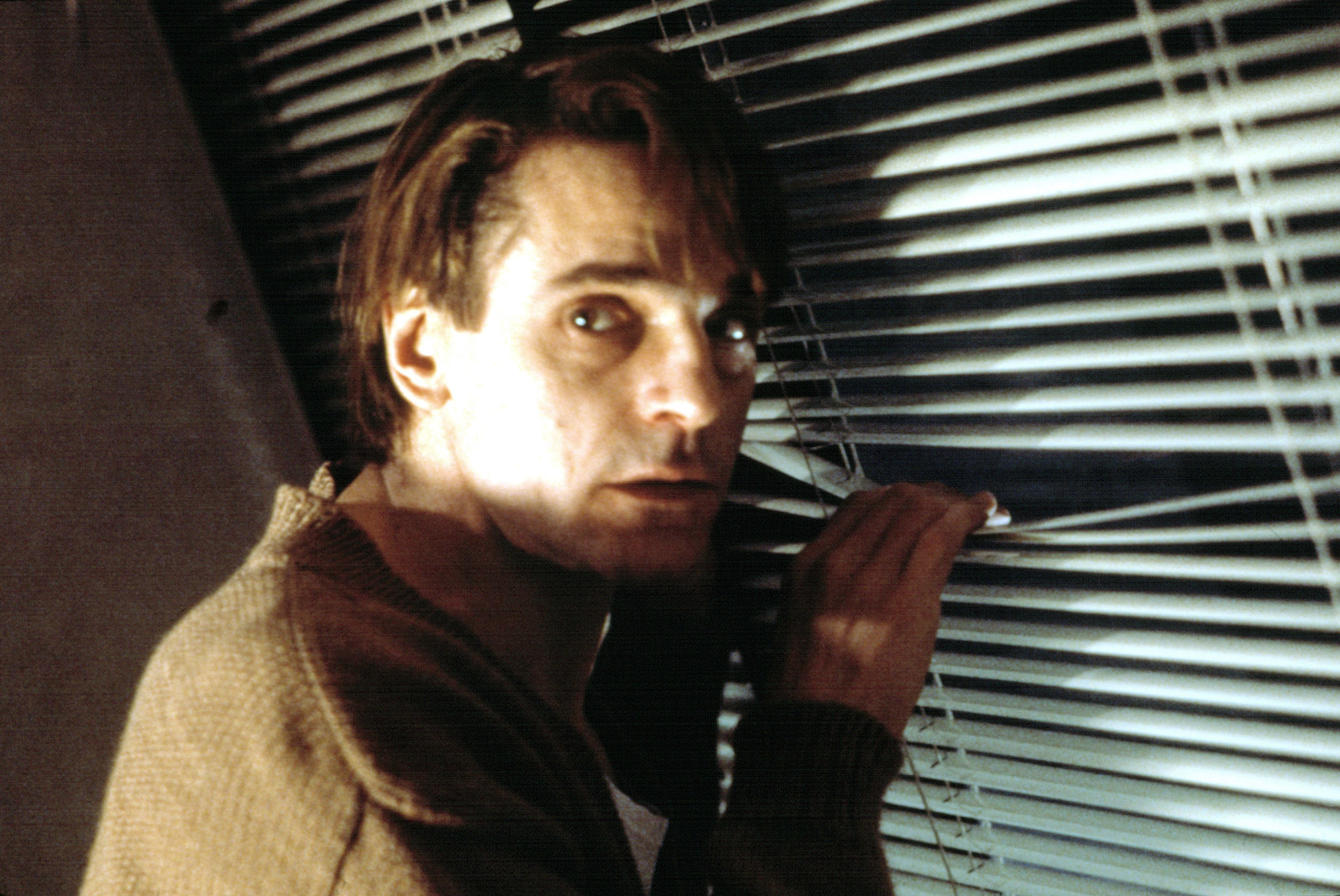 Jeremy Irons looking through Venetian blinds