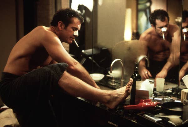 Mel Gibson shaving his legs in the sink and wearing a Biore nose strip while smoking a cigarette