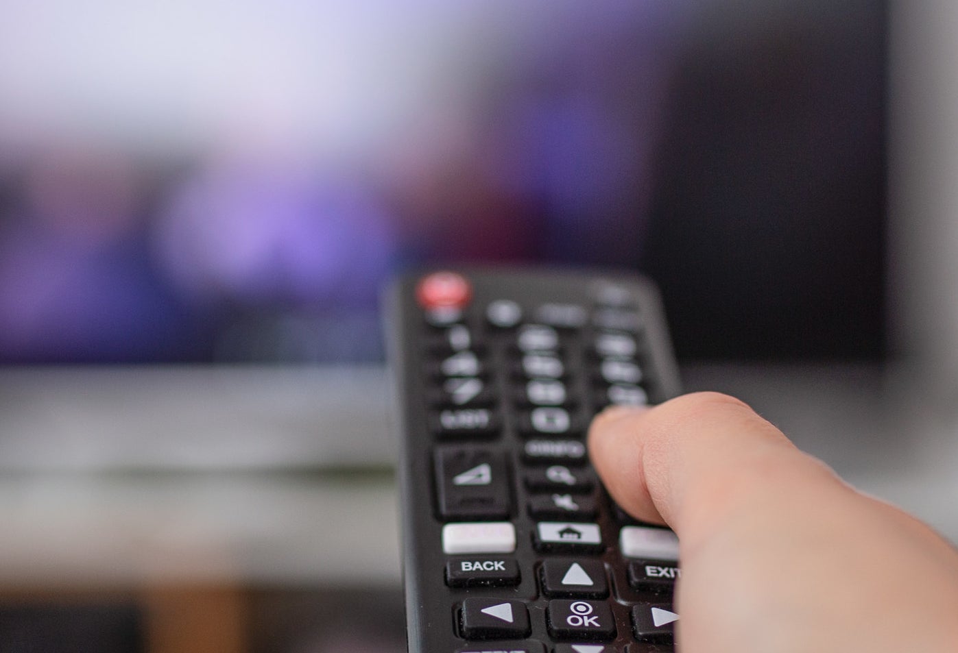 hand pointing remote at out of focus tv screen