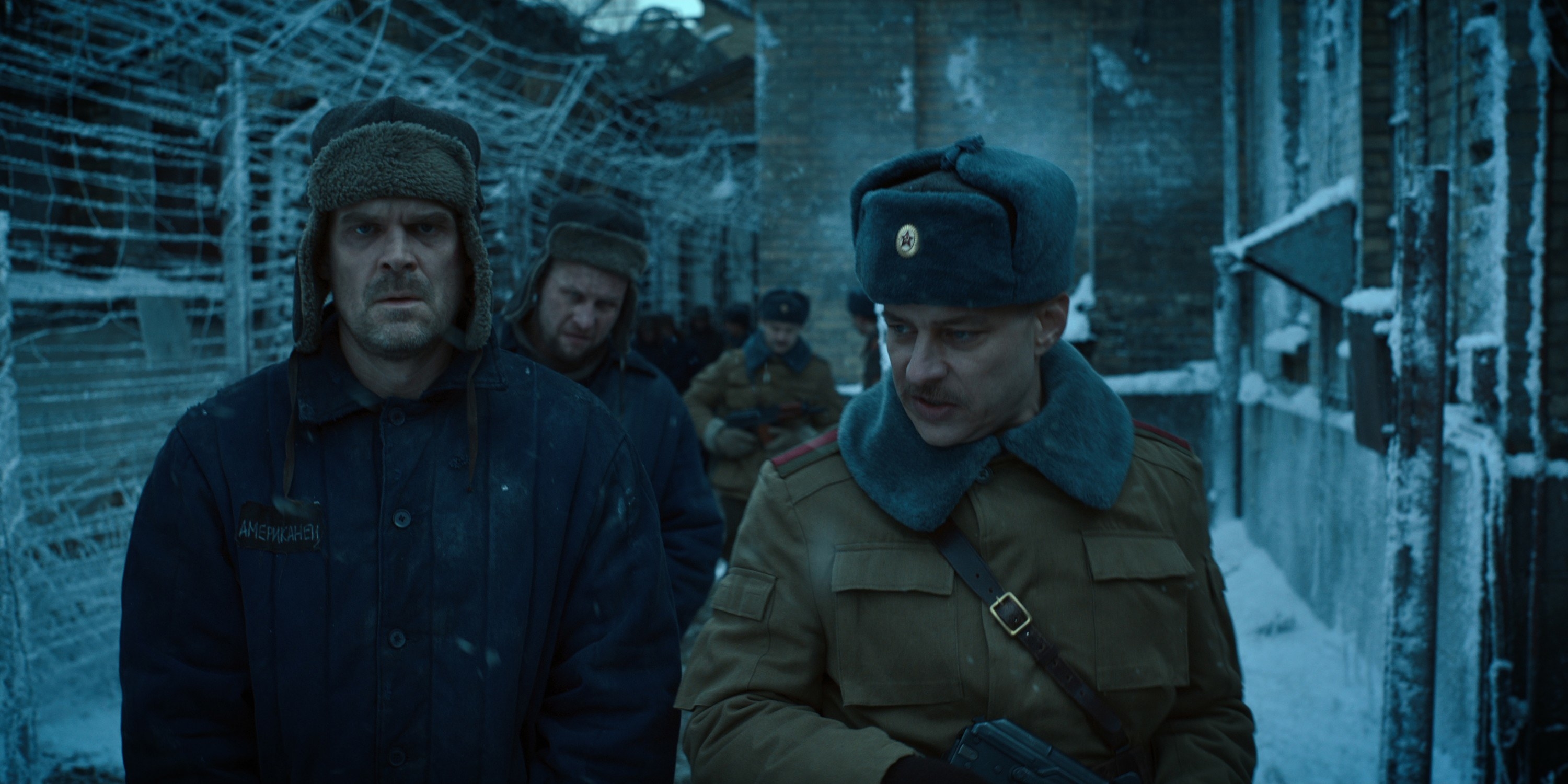 Jim in a Russian-style hat (with ear flaps) in an icy, prisonlike setting