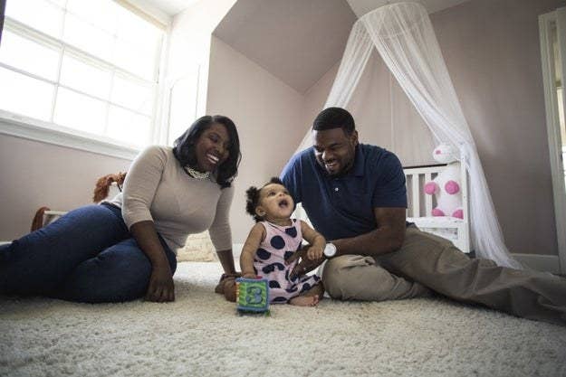 A couple sits and laughs with their baby in her nursery